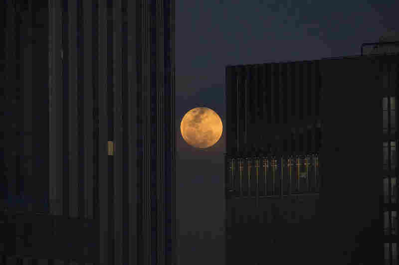 The moon rises between two office buildings in Bangkok. 