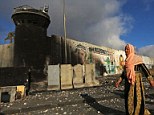 A Palestinian woman walks on a street full of stones which were hurled in clashes between Palestinians and Israeli security forces in front of an Israeli watch tower of the Qalandia checkpoint near the West Bank city of Ramallah