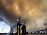 Police officers direct traffic under a cloud of smoke from a wildfire in Fort McMurray, Alberta, Canada on Friday, May 6, 2016. Tens of thousands have been forced from their homes, and the fires are expected to burn for weeks. (Jason Franson/The Canadian Press via AP) MANDATORY CREDIT