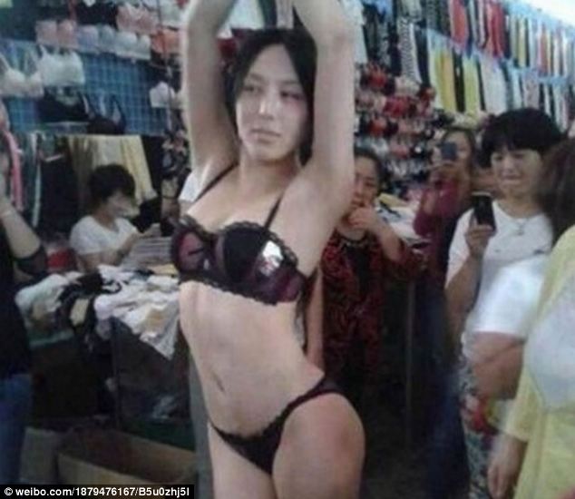 Suits you: The business woman strikes another pose as she advertises another set of underwear while shoppers take photos on their mobile phones in the background