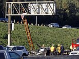 The body of a driver ejected when his car rolled over several times on southbound Interstate 5 is seen where it landed on an overhead freeway sign north of downtown Los Angeles Friday morning, Oct. 30, 2015. California Highway Patrol officers got a ladder and climbed to the body, covered it and waited for a coroner's representative. The victim was described as a 20-year-old male. The wreckage of the car came to rest under the sign.(AP Photo/Nick Ut)