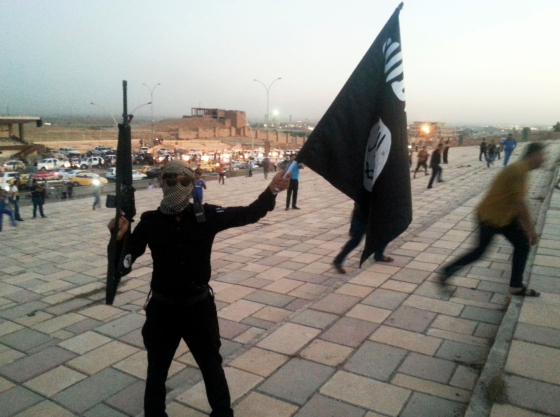 A fighter of the ISIL holds a flag and a weapon on a street in Mosul