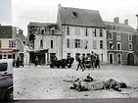 The body of a German soldier belonging lies on the Market Square in Trevieres, 15 June, 1944. The two jeeps in the centre of the photo and the two GIs at the left are part of the MP Platoon of the 2nd Infantry Division