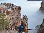 Visitors to Mather Point on the South Rim of Grand Canyon National Park, in Ariz., view a rare weather phenomenon - a sea of thick clouds filling the canyon just below the rim, Thursday, Dec. 11, 2014. The total cloud inversion is expected to hang inside the canyon throughout Thursday. Cory Mottice of the National Weather Service said the weather event happens about once every several years, though the landmark was treated to one last year. (AP Photo/National Park Service, Michael Quinn)