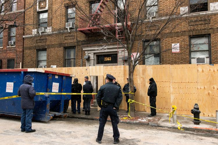 Snow falls on Saturday morning as police officers guard the boarded-up building at 2363 Prospect Ave. where 12 perished Thursday night. 