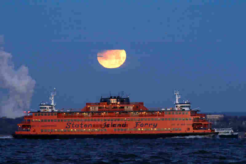 The super blue blood moon sets behind the Staten Island Ferry, as seen from Brooklyn, New York.